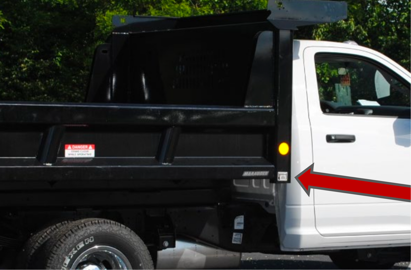 White truck with black dump bed on a road with greenery in the background